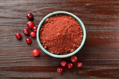 Photo of Dried cranberry powder in bowl and fresh berries on wooden table, top view