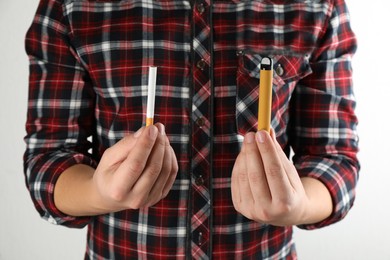 Photo of Man with cigarette and vaping device on light background, closeup. Smoking alternative
