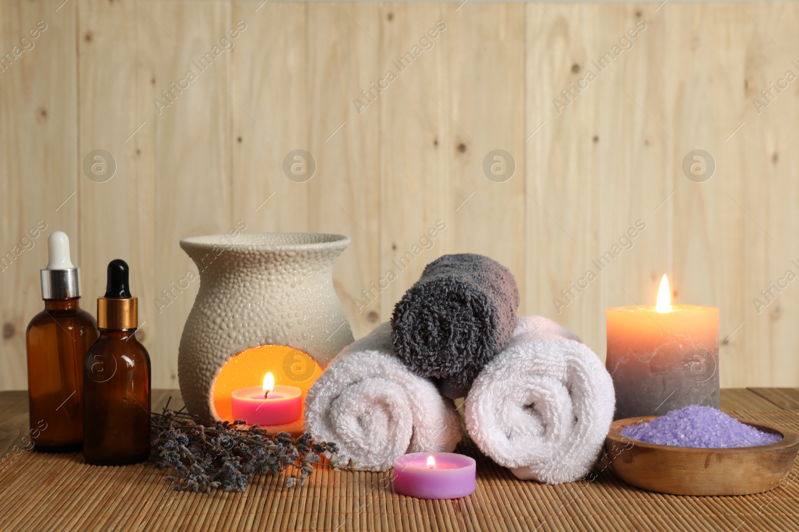 Photo of Aromatherapy. Scented candles, bottles, lavender, towels and sea salt on bamboo mat