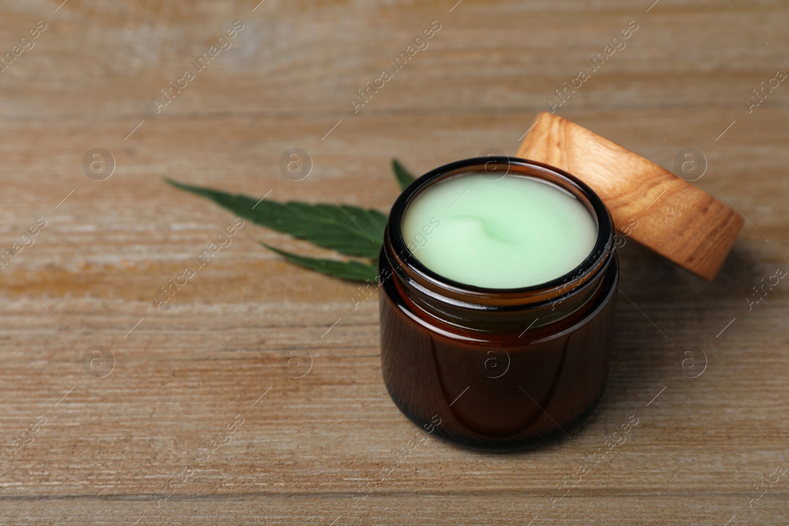 Photo of Jar of hemp cream and leaf on wooden table, space for text. Natural cosmetics