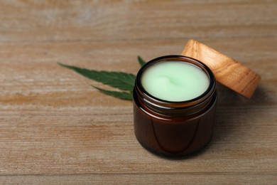 Photo of Jar of hemp cream and leaf on wooden table, space for text. Natural cosmetics