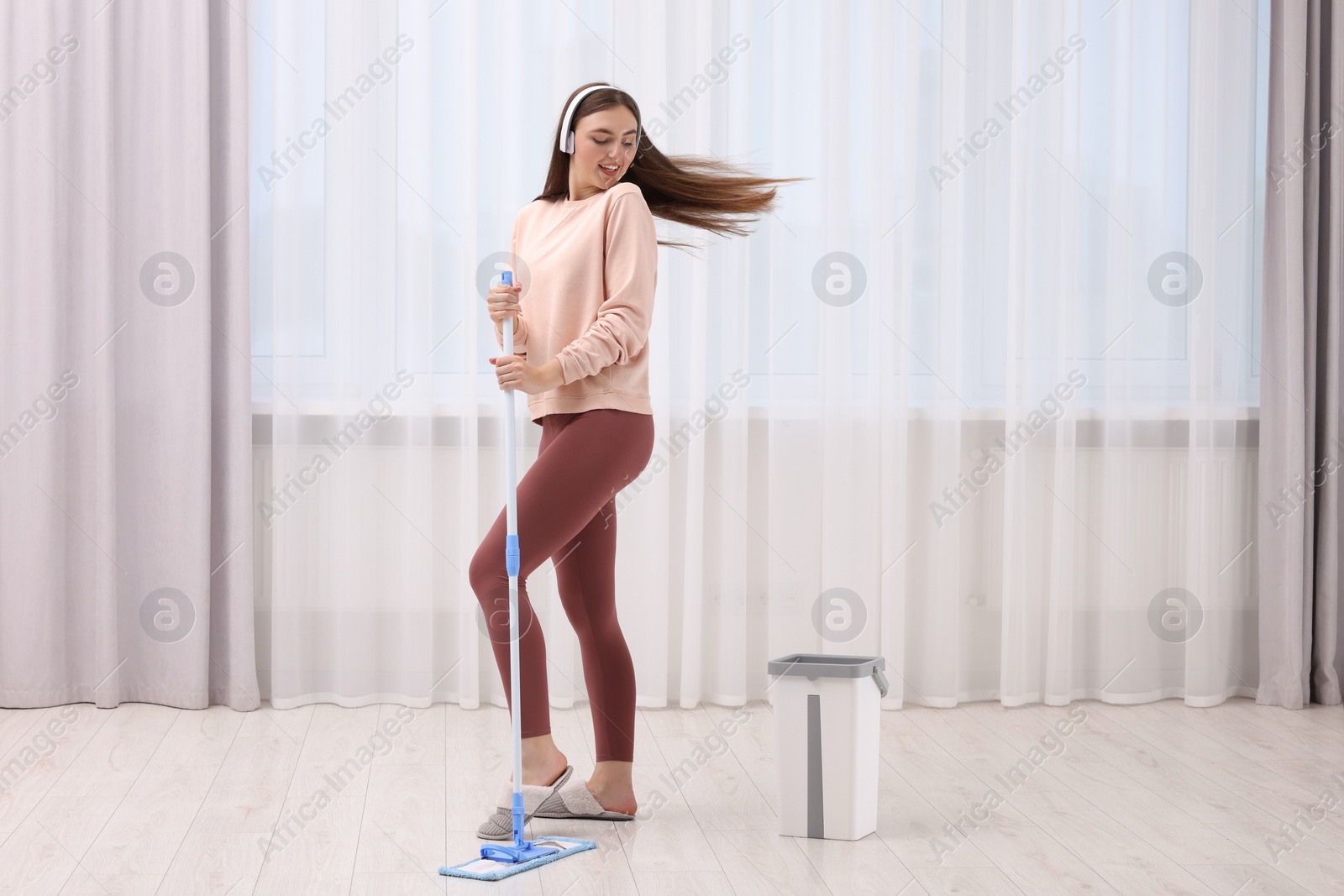 Photo of Enjoying cleaning. Happy woman in headphones listening music with mop indoors. Space for text