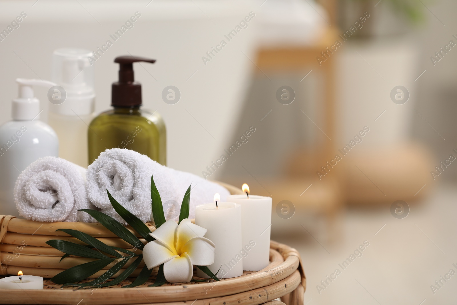 Photo of Spa products, burning candles, plumeria flower and tropical leaf on table in bathroom. Space for text