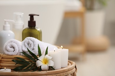 Spa products, burning candles, plumeria flower and tropical leaf on table in bathroom. Space for text