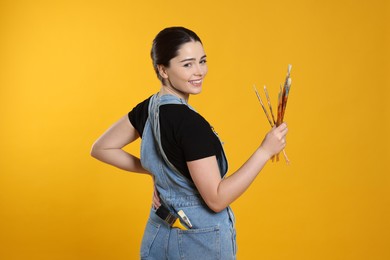 Photo of Woman with paintbrushes on yellow background. Young artist