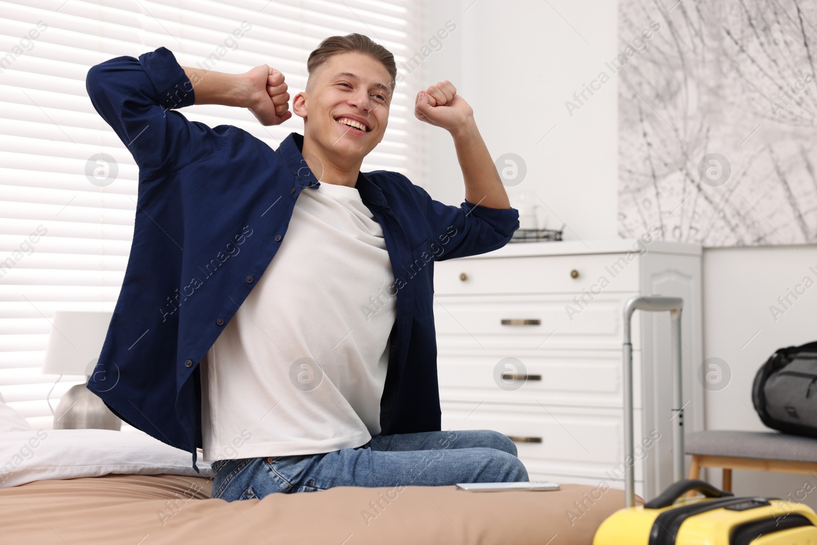 Photo of Smiling guest stretching on bed in stylish hotel room