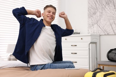 Photo of Smiling guest stretching on bed in stylish hotel room