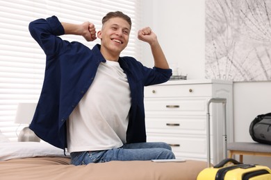 Smiling guest stretching on bed in stylish hotel room