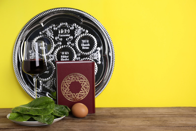 Photo of Symbolic Pesach (Passover Seder) items on wooden table against yellow background, space for text