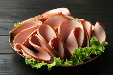 Photo of Slices of delicious boiled sausage with lettuce on dark wooden table, closeup