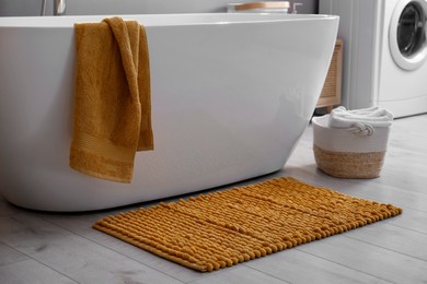 Photo of Soft orange mat on floor near tub in bathroom. Interior design