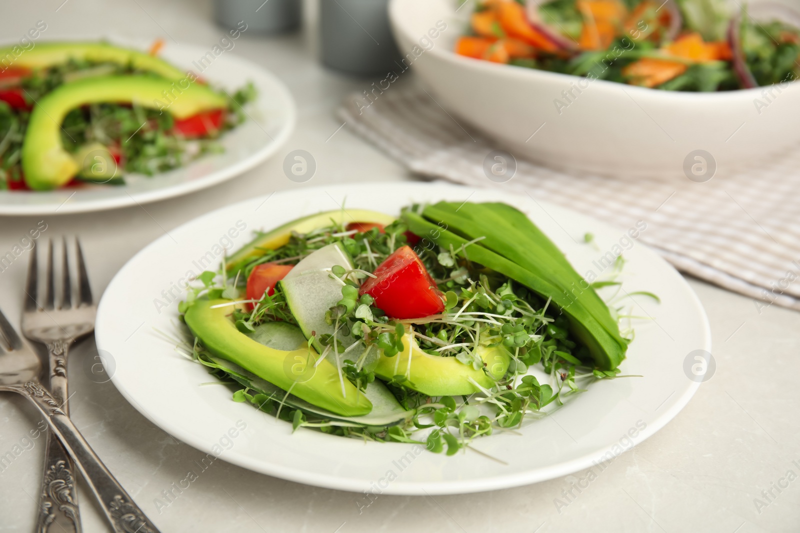 Photo of Delicious vegetable salad with avocado and microgreen served on light table