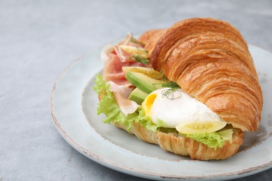 Photo of Delicious croissant with prosciutto, avocado and egg on grey table, closeup. Space for text