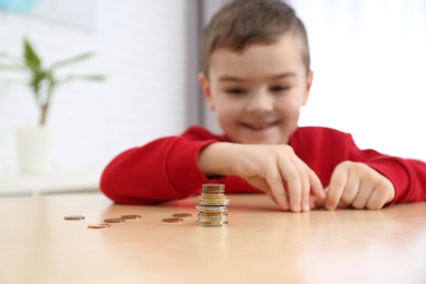 Cute little boy with coins at home, closeup. Counting money