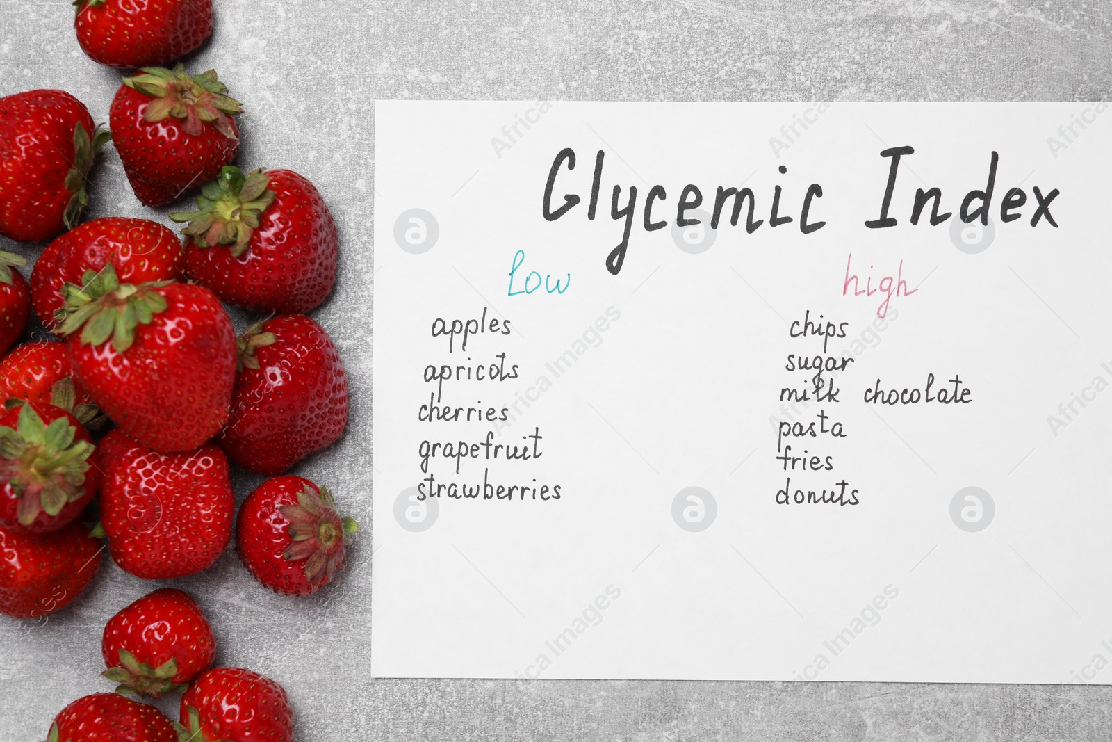 Photo of List with products of low and high glycemic index and strawberries on light grey table, top view