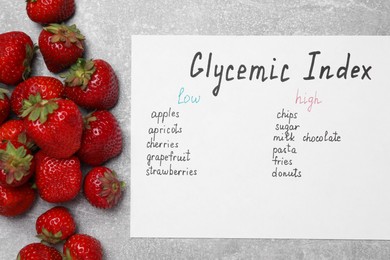 Photo of List with products of low and high glycemic index and strawberries on light grey table, top view
