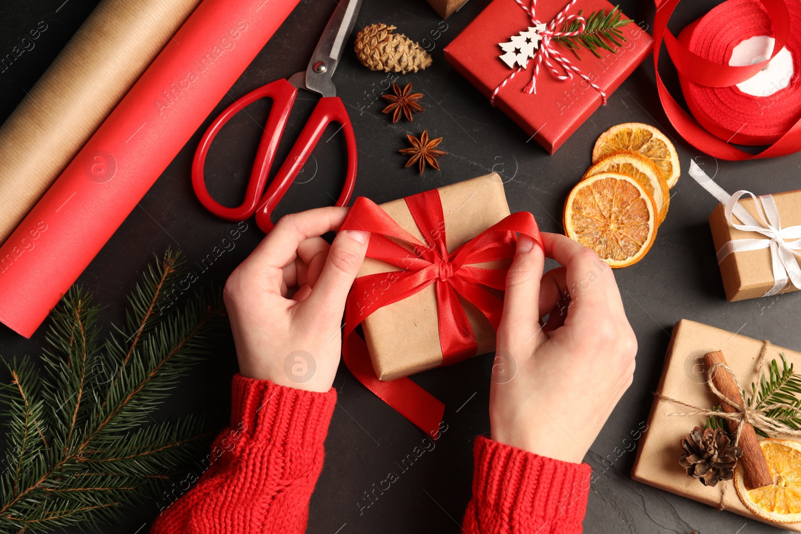 Photo of Woman decorating gift box on black table, top view. Christmas present