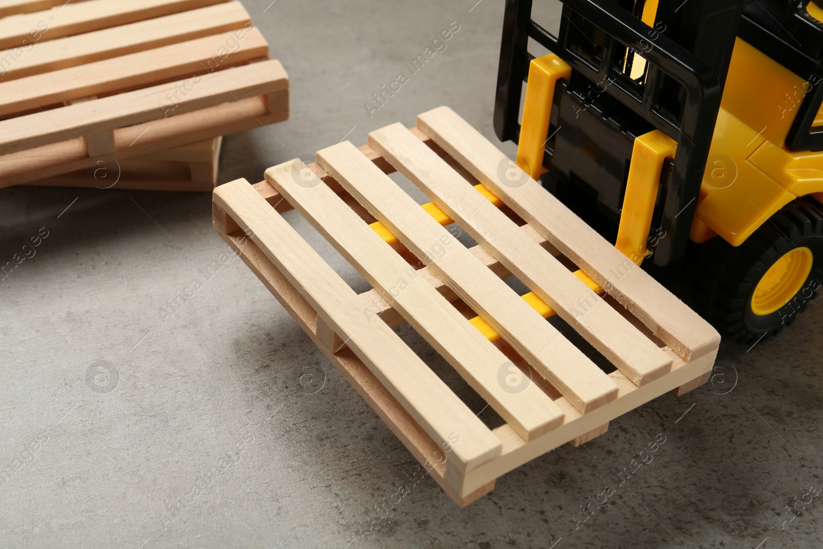 Photo of Toy forklift and wooden pallets on light grey table, closeup