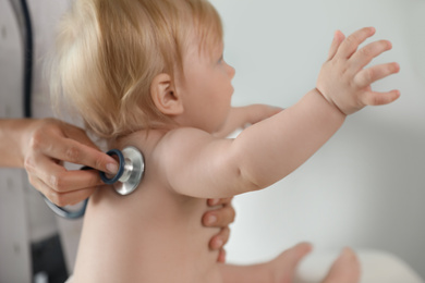 Photo of Pediatrician examining baby with stethoscope in hospital, closeup. Health care