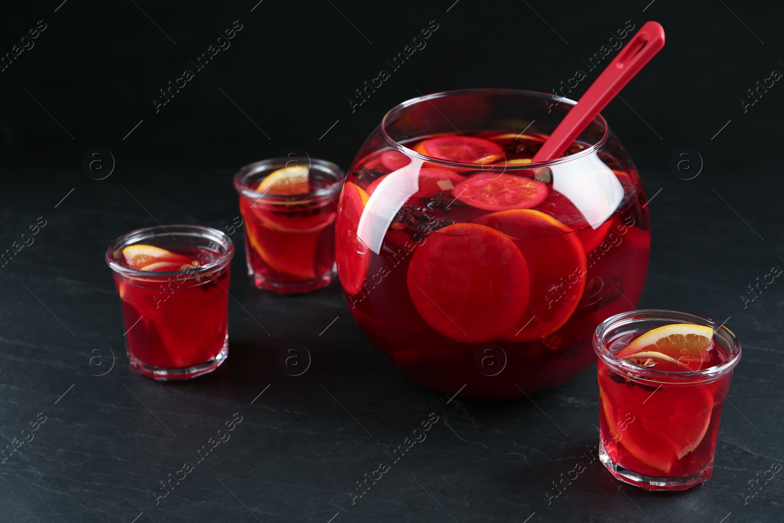 Photo of Glasses and bowl of delicious aromatic punch drink on black table