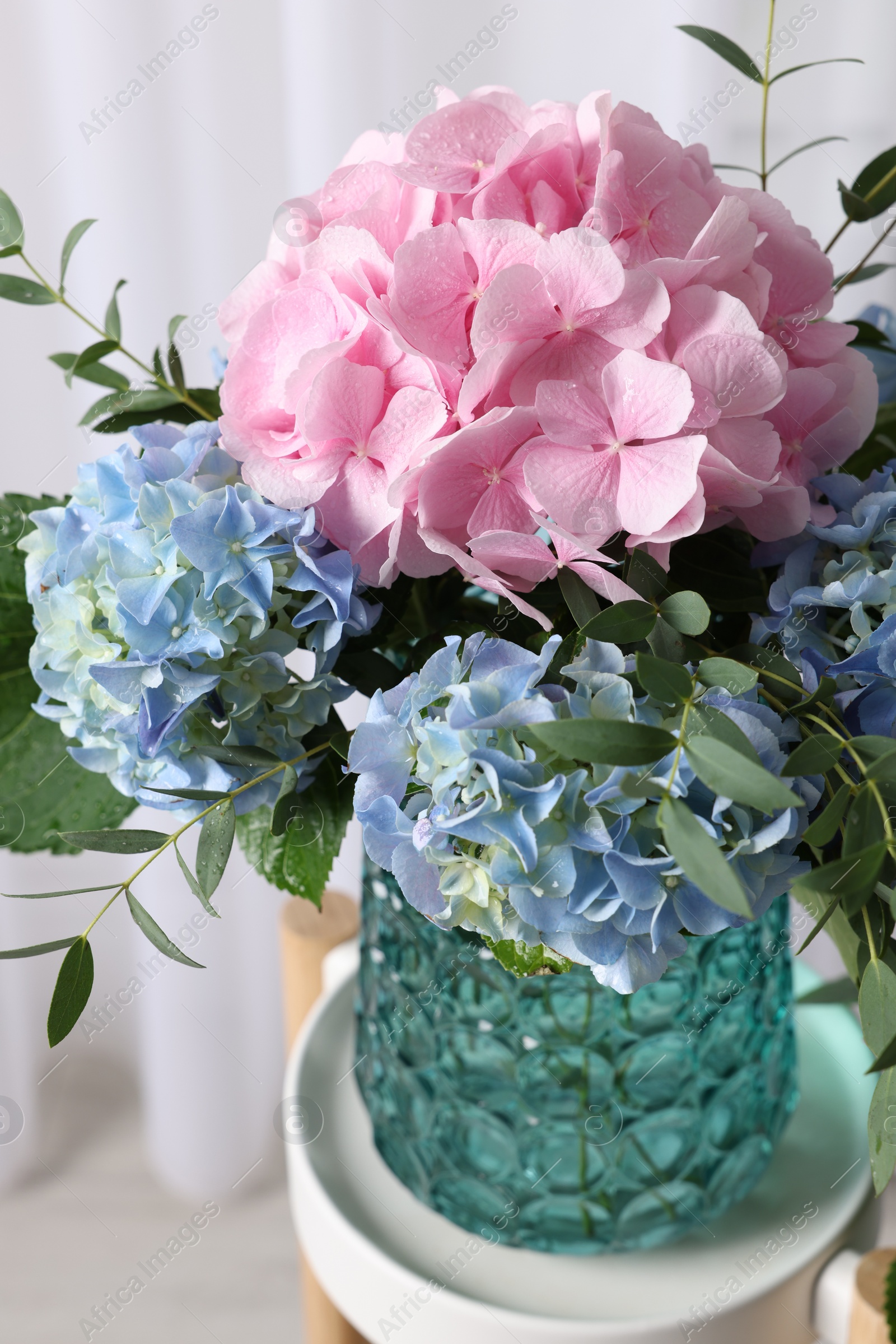 Photo of Beautiful hortensia flowers in vase on stand indoors