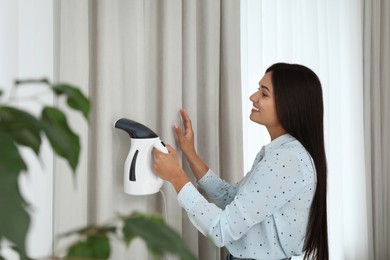 Photo of Woman steaming curtain near window at home