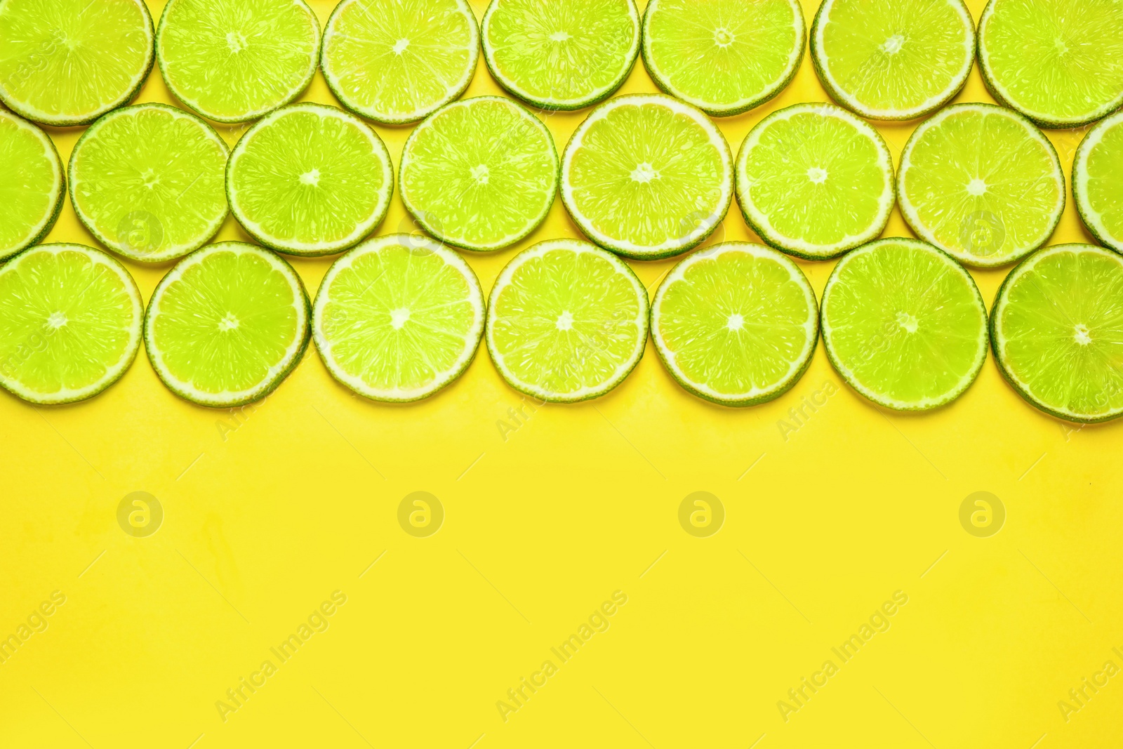 Photo of Juicy fresh lime slices on yellow background, flat lay. Space for text