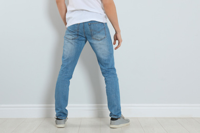 Photo of Young man in stylish jeans near light wall, closeup