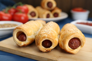 Photo of Delicious sausage rolls and ingredients on blue wooden table, closeup
