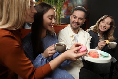 People with coffee and macarons spending time together in cafe