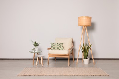 Stylish armchair, floor lamp and plants near white wall. Interior design