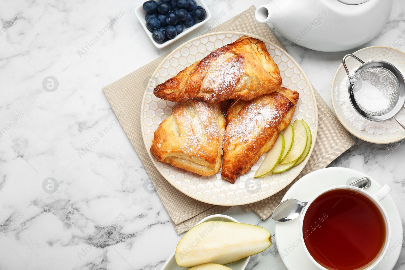 Photo of Fresh tasty puff pastry with sugar powder, pear, blueberries and aromatic tea served on white marble table, flat lay. Space for text