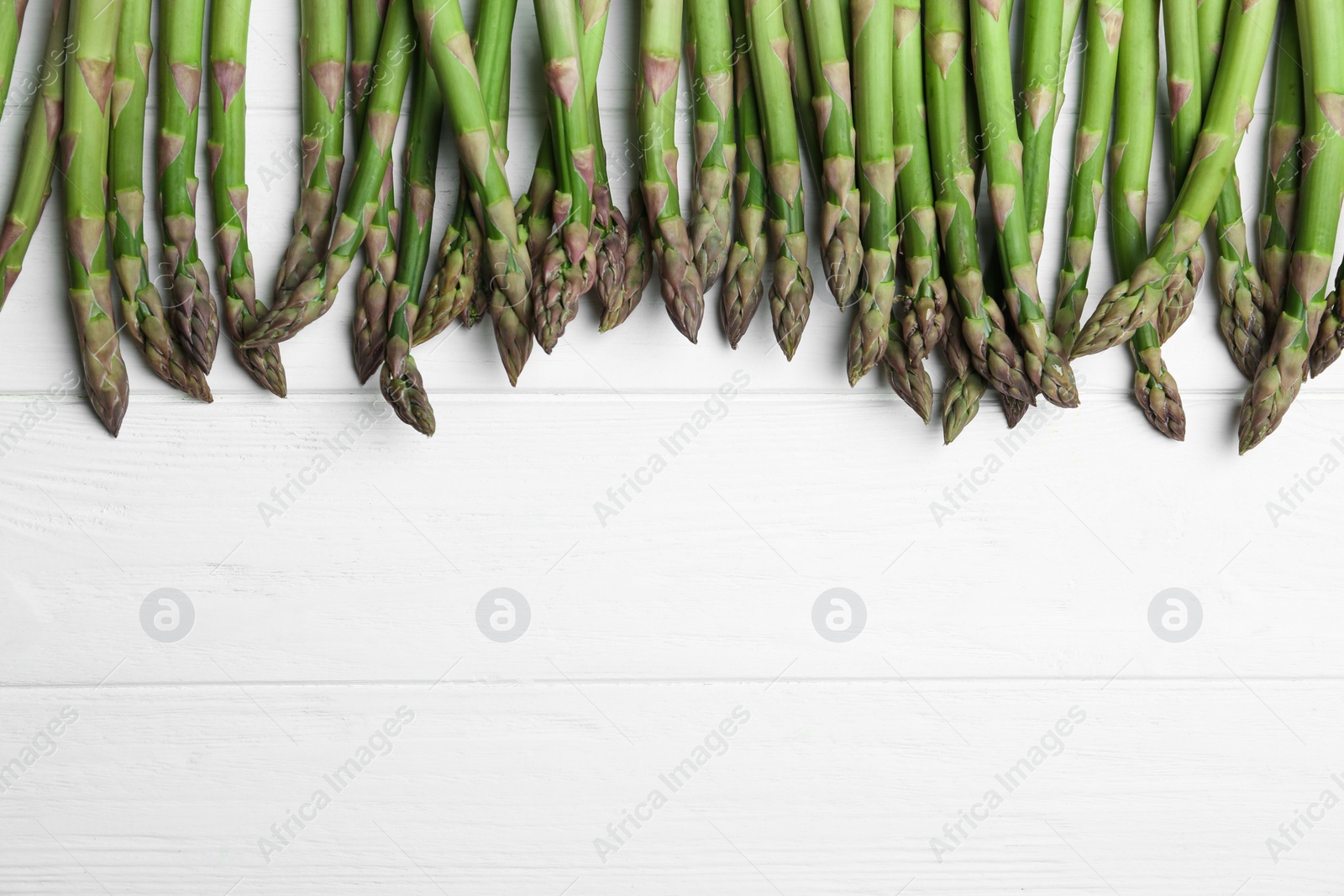 Photo of Fresh raw asparagus on white table, flat lay. Space for text