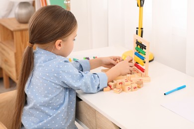 Cute little girl playing with wooden cubes at desk in room. Home workplace