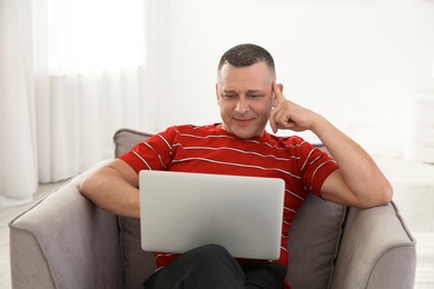 Photo of Mature man with laptop sitting in armchair at home