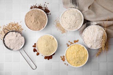 Photo of Bowls with different types of flour and seeds on tiled table, flat lay