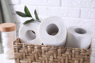 Photo of Toilet paper rolls in wicker basket, floral decor and cotton pads on table