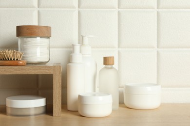 Photo of Different bath accessories and personal care products on wooden table near white tiled wall