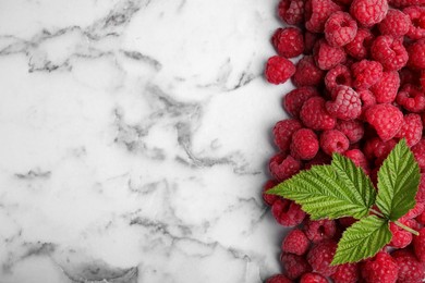 Photo of Fresh ripe raspberries with green leaves on white marble table, flat lay. Space for text