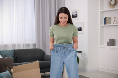 Photo of Happy woman with stylish light blue jeans at home. Online shopping