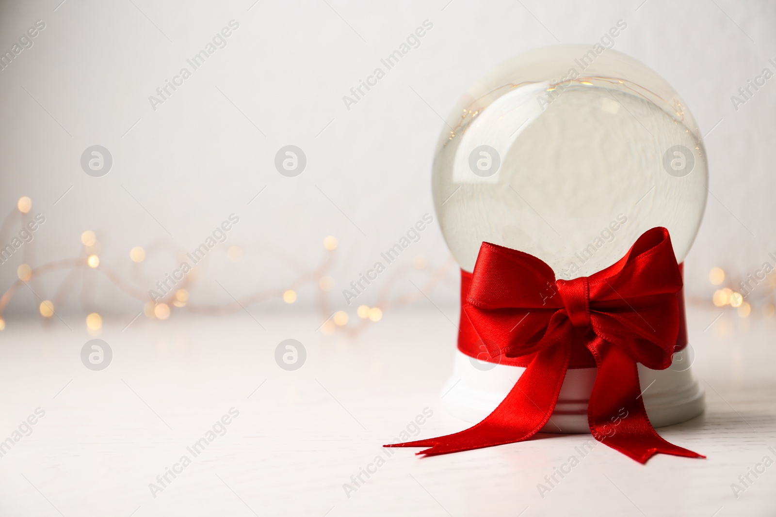 Photo of Beautiful Christmas snow globe with red bow on table against light background, space for text