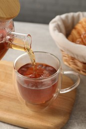 Photo of Pouring aromatic tea into glass cup at table, closeup