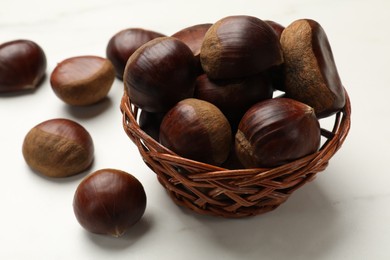 Sweet fresh edible chestnuts in wicker bowl on white table, closeup