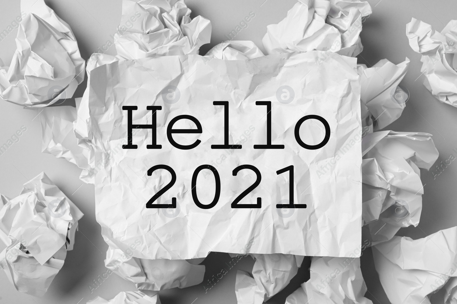 Image of Crumpled sheet with phrase Hello 2021 among paper balls on light grey table, flat lay