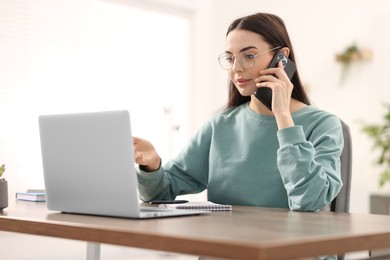 Photo of Young woman talking on smartphone during webinar at table in room