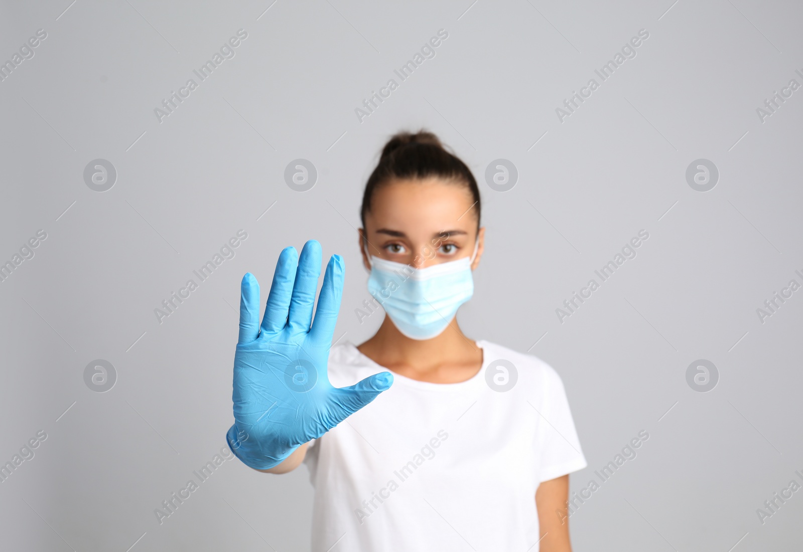 Photo of Woman in protective mask showing stop gesture on grey background. Prevent spreading of COVID‑19
