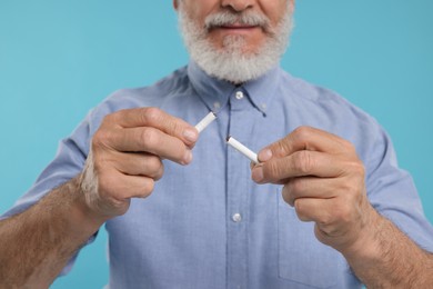 Stop smoking concept. Man holding pieces of broken cigarette on light blue background, closeup
