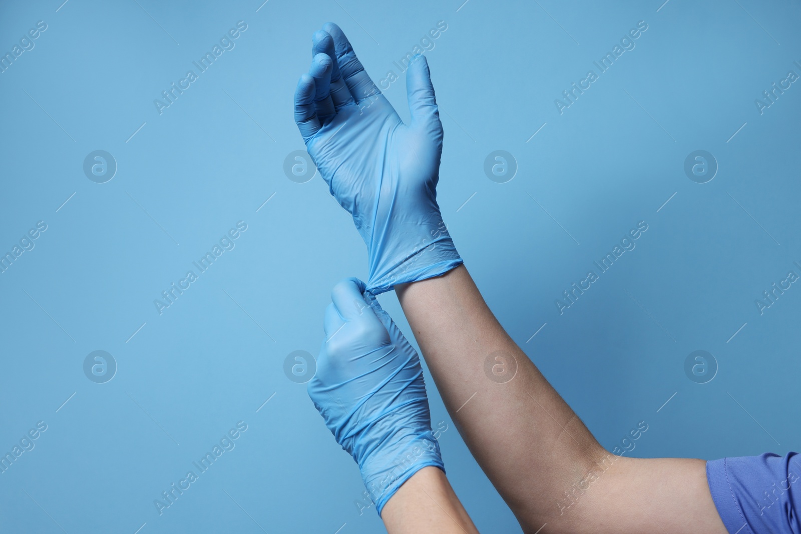 Photo of Doctor wearing medical gloves on light blue background, closeup