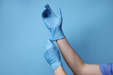 Doctor wearing medical gloves on light blue background, closeup