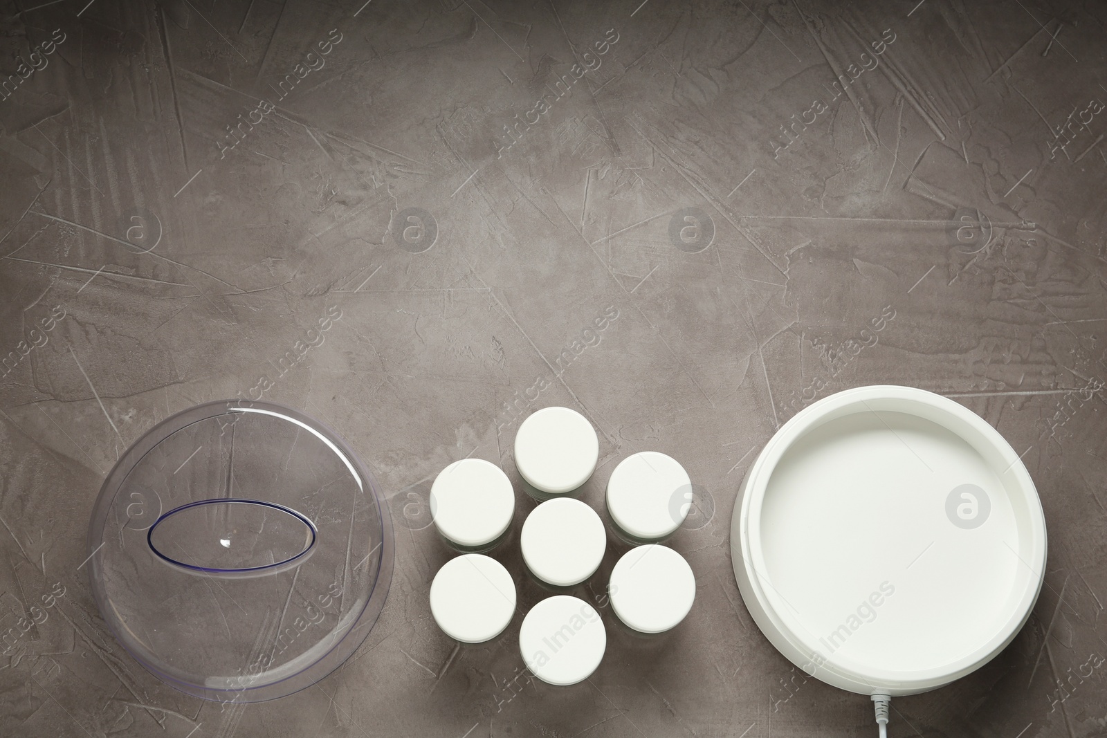 Photo of Modern yogurt maker with jars on grey table, flat lay. Space for text